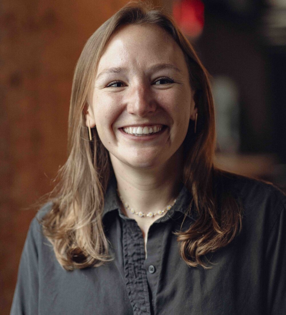 Smiling woman with light brown hair and dark shirt indoors.