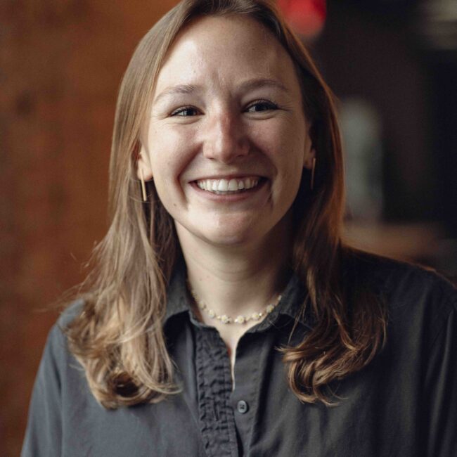Smiling woman with light brown hair and dark shirt indoors.