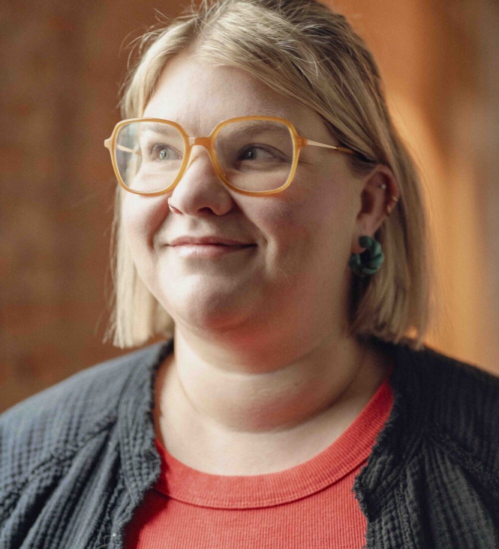 Woman with short blonde hair and orange glasses, smiling upward.