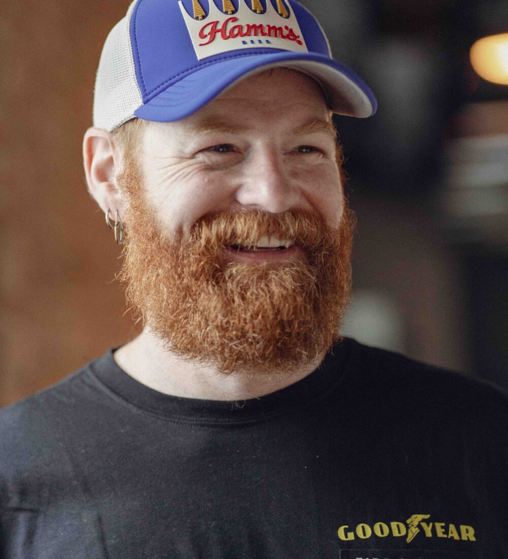 A bearded man in a cap and black Goodyear T-shirt smiles.