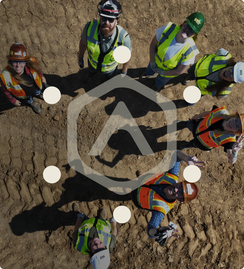Six construction workers in a loose circle look up with overlay logo.
