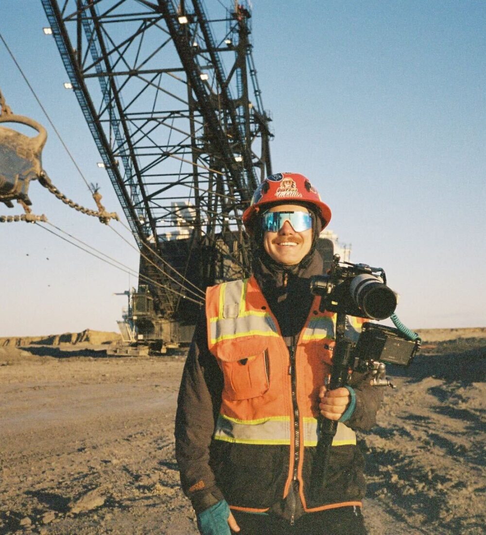 Person in safety gear with camera before large industrial equipment.