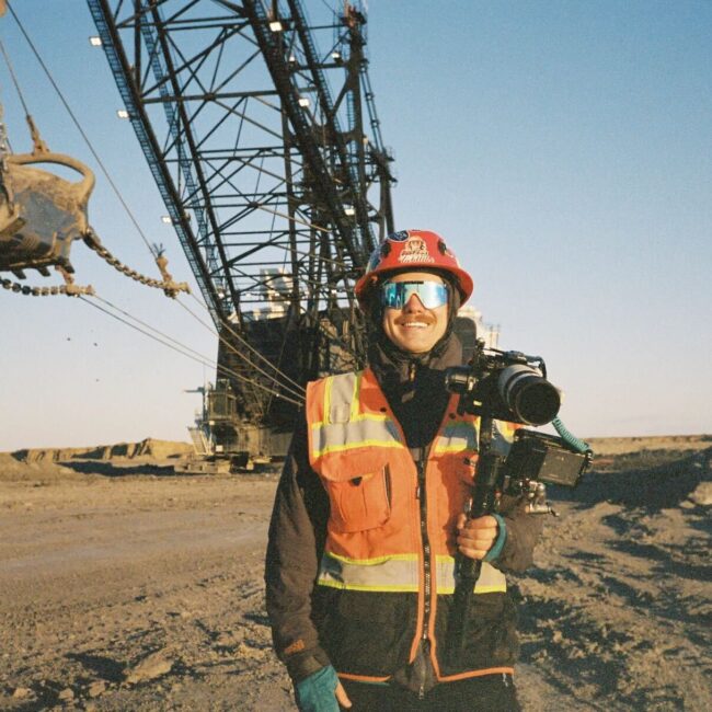 Person in safety gear with camera before large industrial equipment.