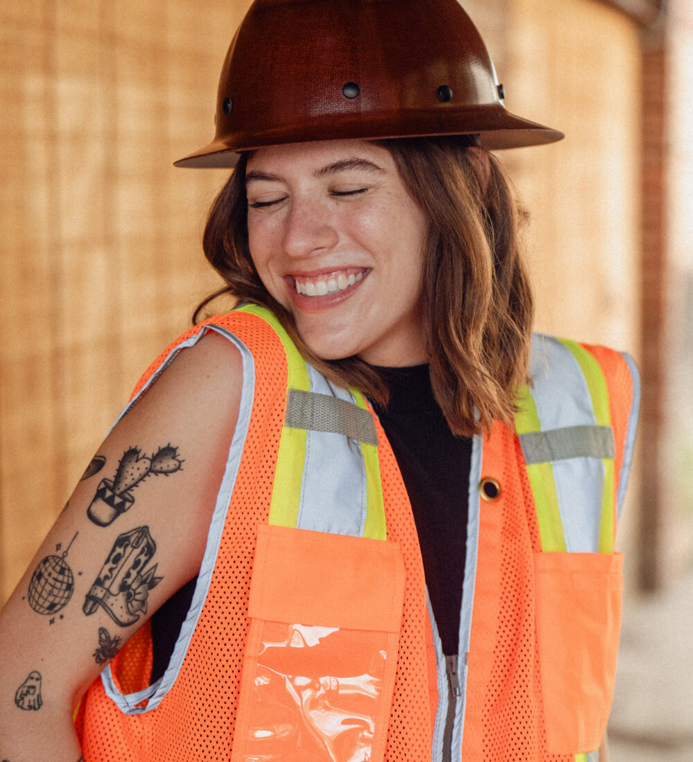 woman in a hard hat and safety vest smiles
