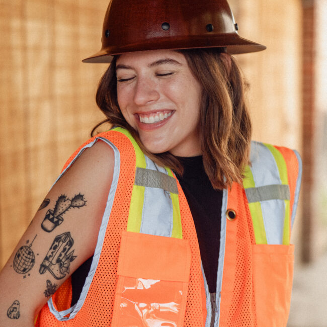 woman in a hard hat and safety vest smiles