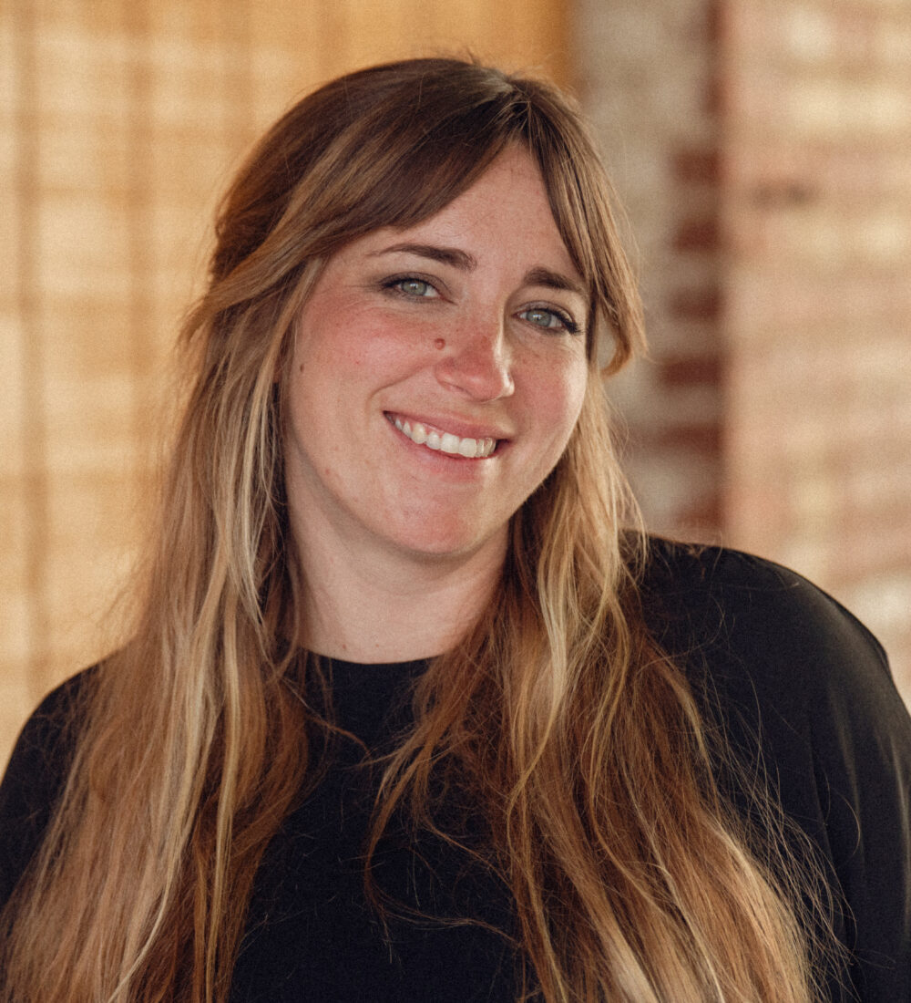 Woman with long brown hair in black top smiling.