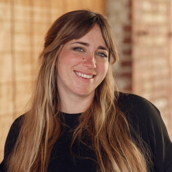 Woman with long brown hair in black top smiling.