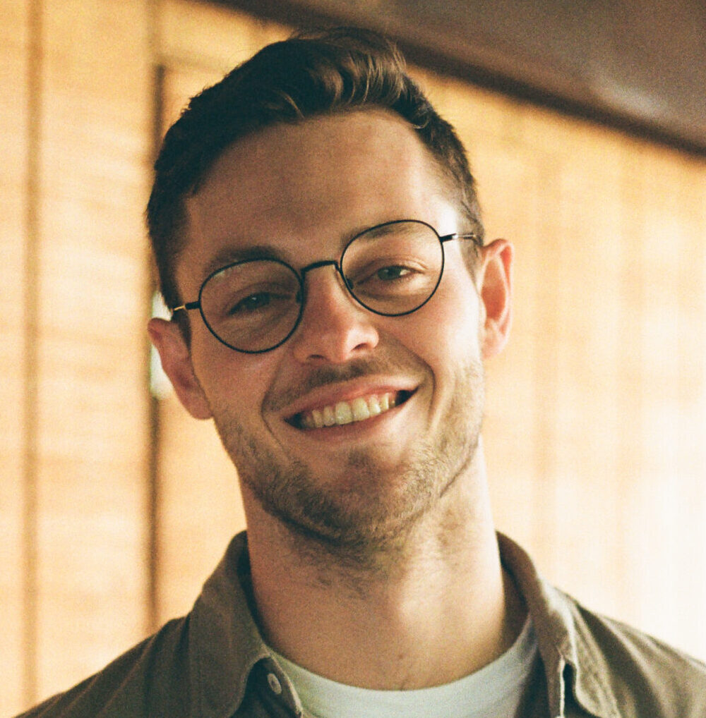 Smiling man with glasses, facial hair, light shirt.