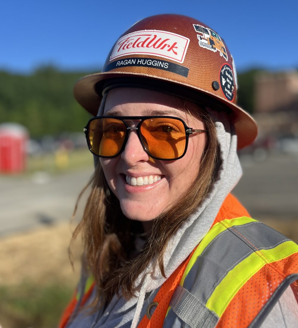 Smiling person in hard hat and safety vest at construction site.