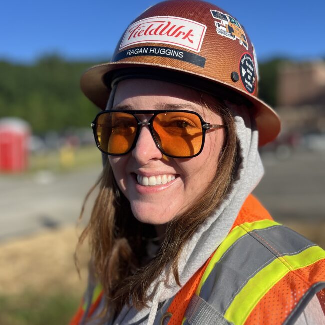 Smiling person in hard hat and safety vest at construction site.