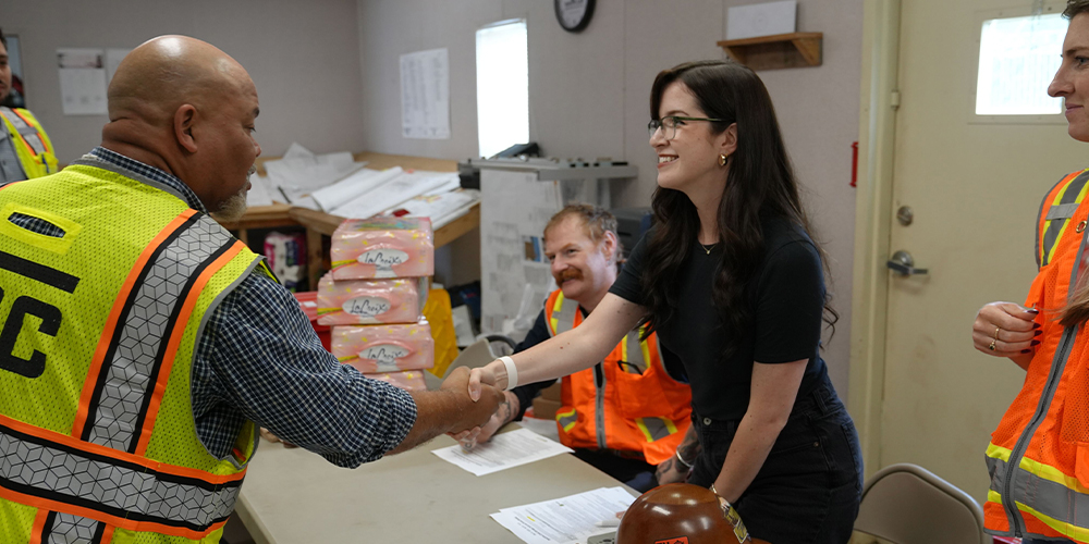 Woman in black shakes hands with man in safety vest at table.