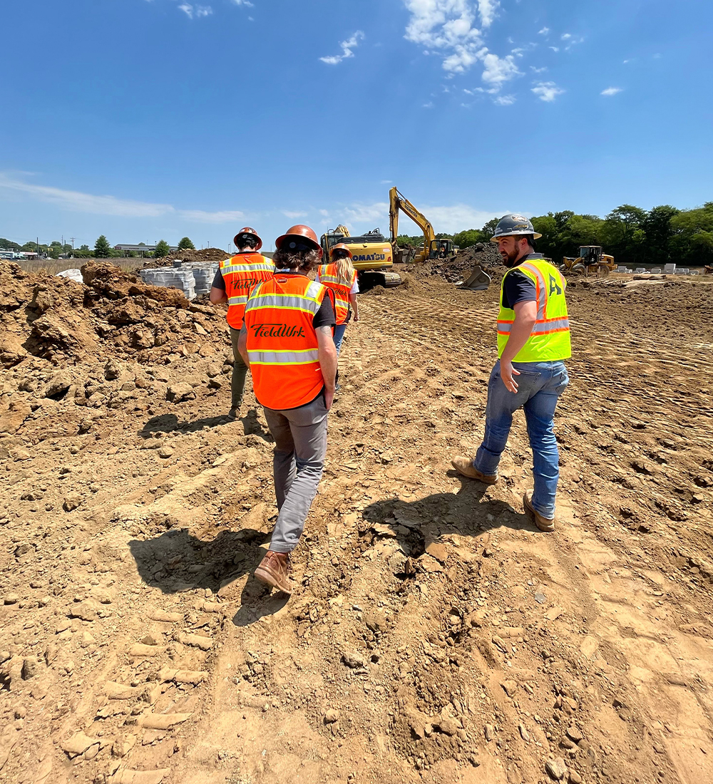 Three construction workers in safety gear walk at a site.