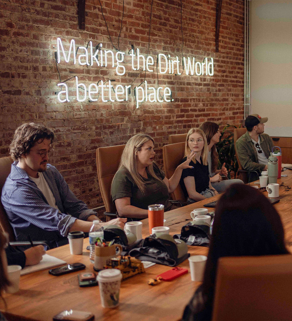 People at conference table with neon sign on brick wall.