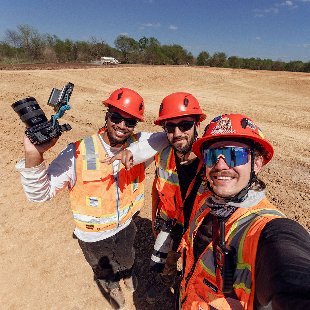 Three men in safety gear take a selfie at construction site.