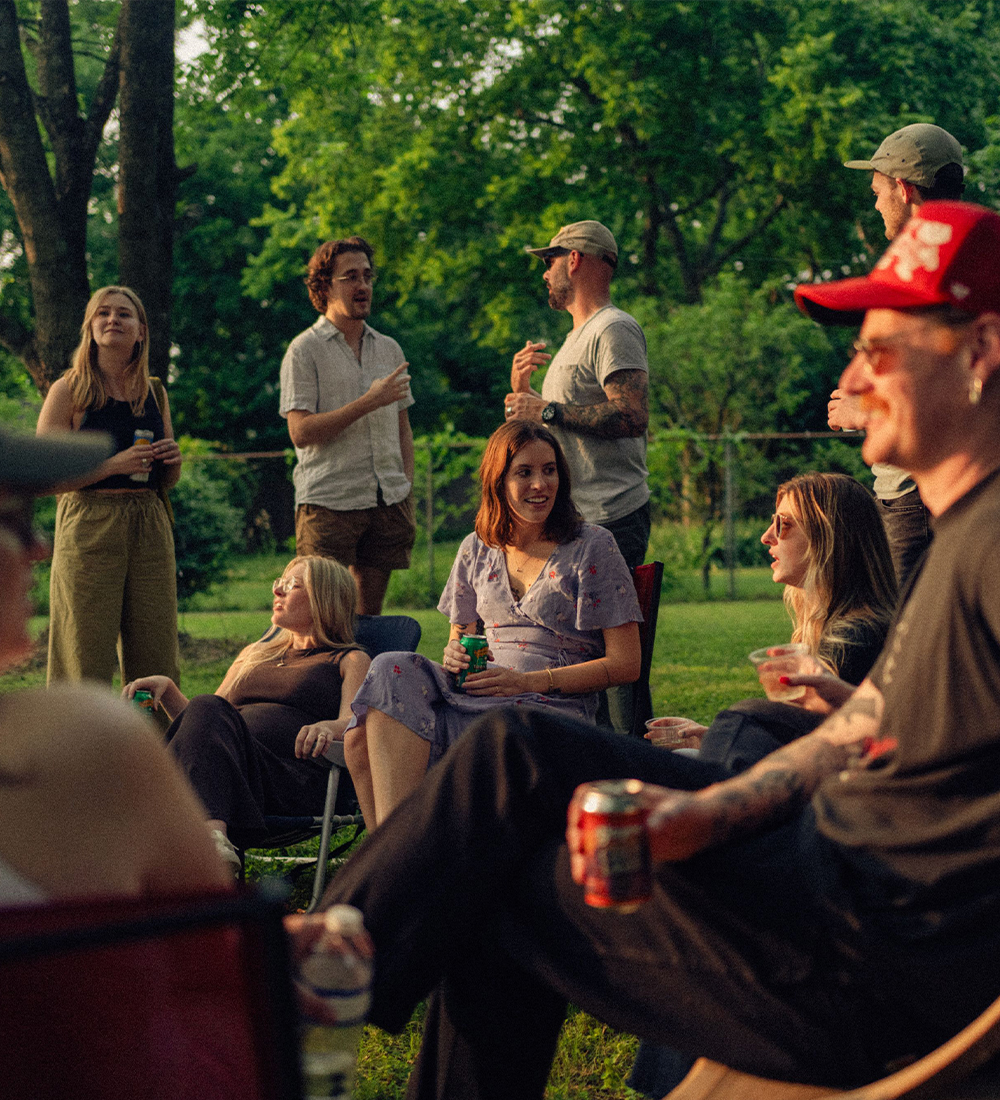 People socialize outdoors among green trees and grass.