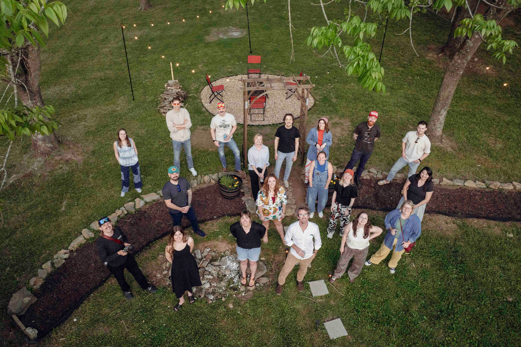 Group poses outdoors with fire pit and string lights.