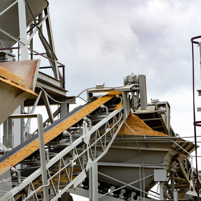 Conveyor system moves grain at facility under cloudy sky.