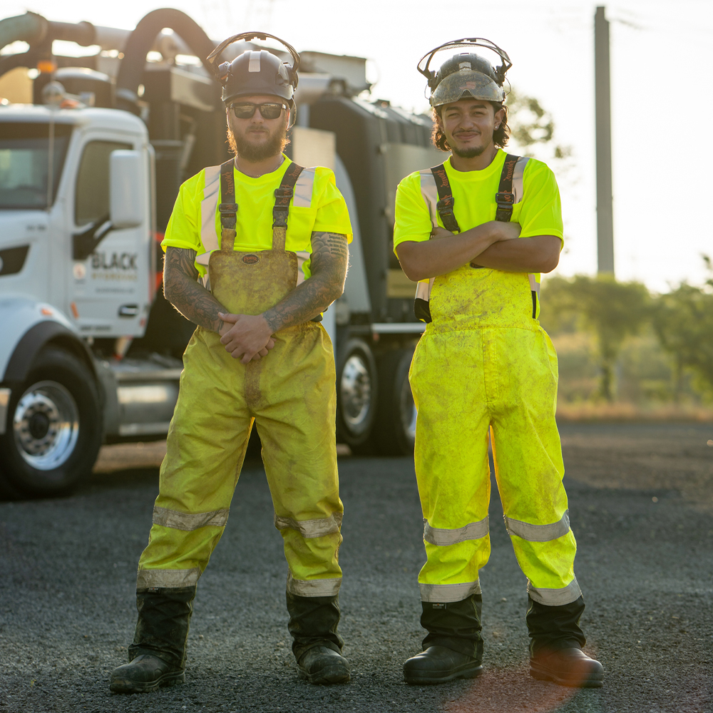 Two workers in yellow safety gear stand by a utility truck outside.
