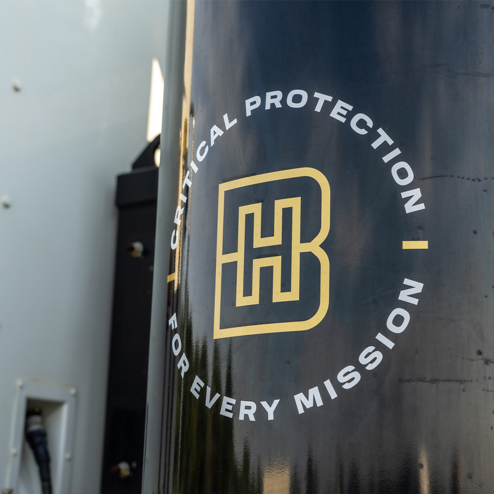 Black cylinder with gold HB logo and circular mission slogan.