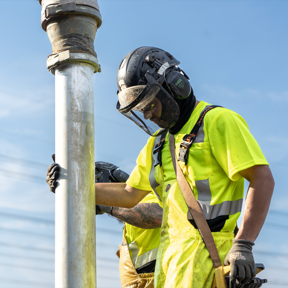 Construction worker in safety gear handles large metal pipe outside.