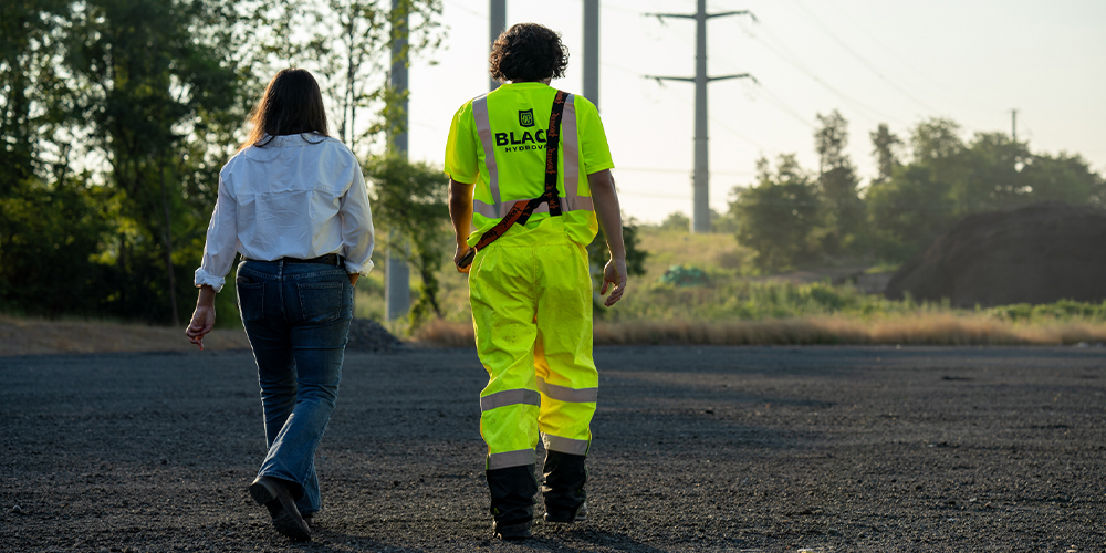 Two people walk on a gravel path near power lines.