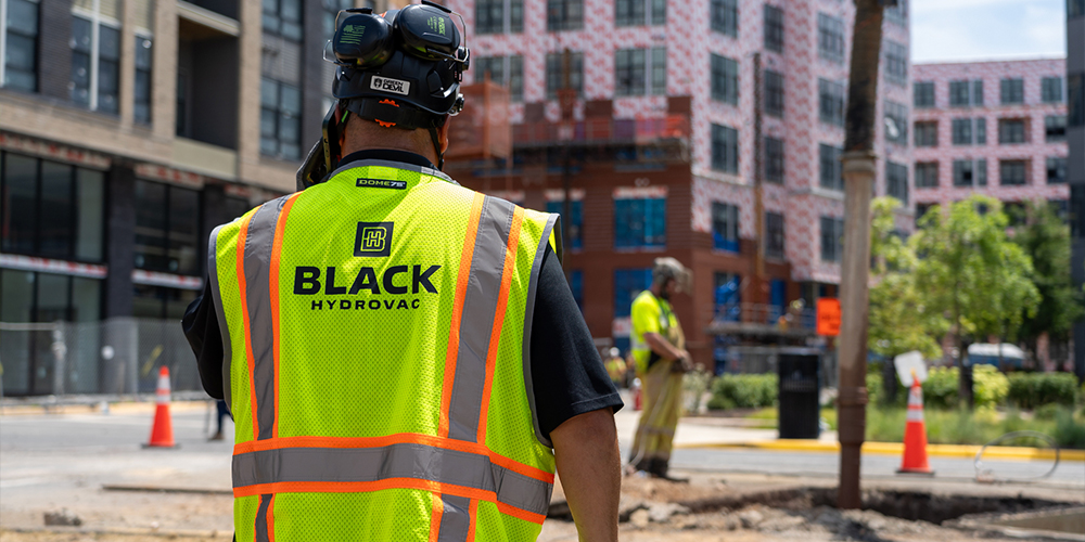 Worker in neon “BLACK HYDROVAC” vest stands at worksite.