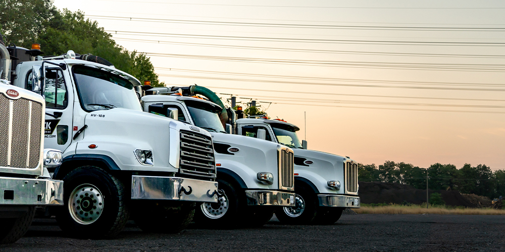 Three white semi-trucks parked side by side at sunset.