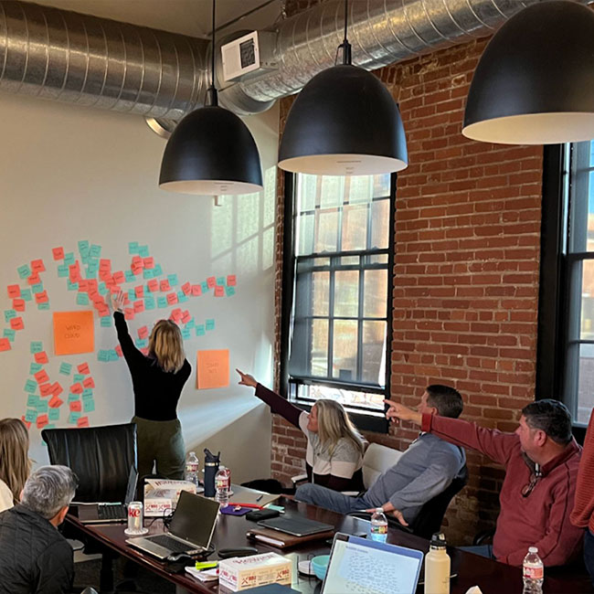 People in a meeting room watch a woman add sticky notes.