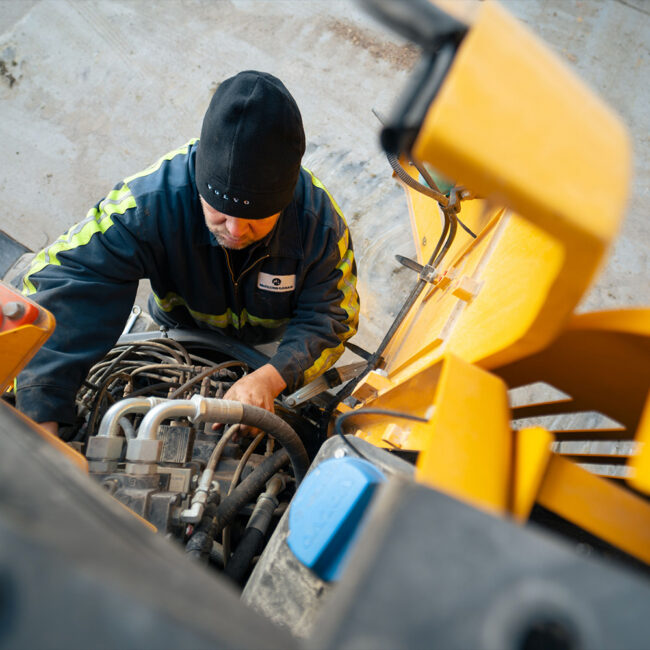 Worker in beanie and safety jacket repairs machinery.