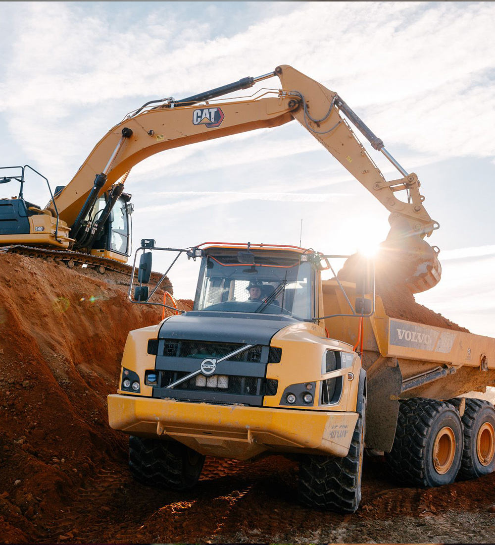 Yellow excavator loading dirt into yellow dump truck outdoors.