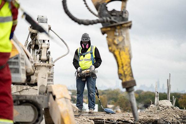 Construction worker in safety gear operates machinery on dusty site.