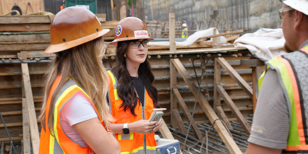 Three workers in hard hats talk at a construction site.