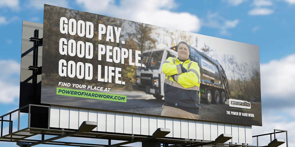 Worker in hi-vis jacket by truck; billboard: “Good pay. Good people. Good life.”