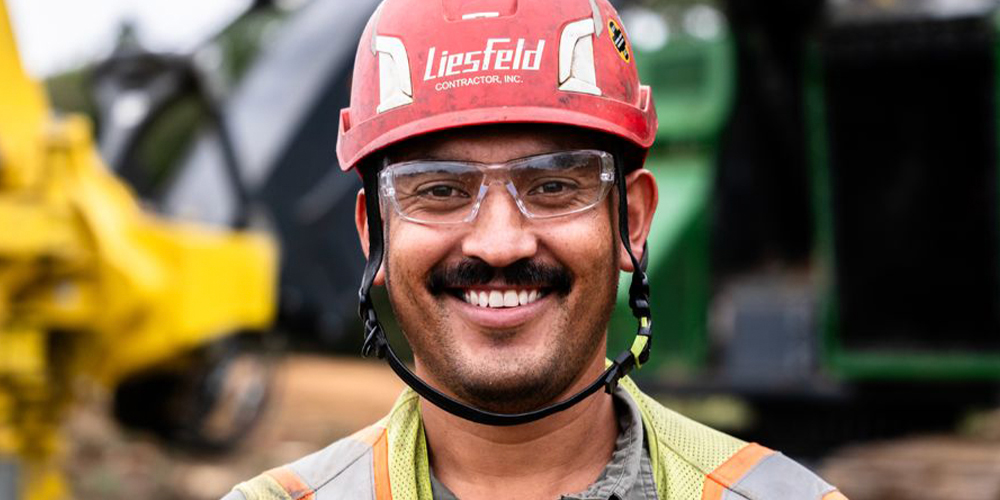 Smiling construction worker in red hard hat and safety vest.