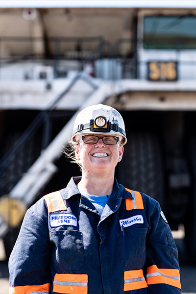 Smiling worker in safety gear stands before mining equipment.