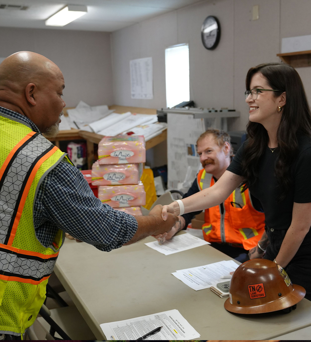 Man in safety vest shakes hands with woman at office table.