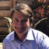 Man with brown hair smiling in a garden.