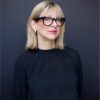 Woman in black glasses poses for headshot.