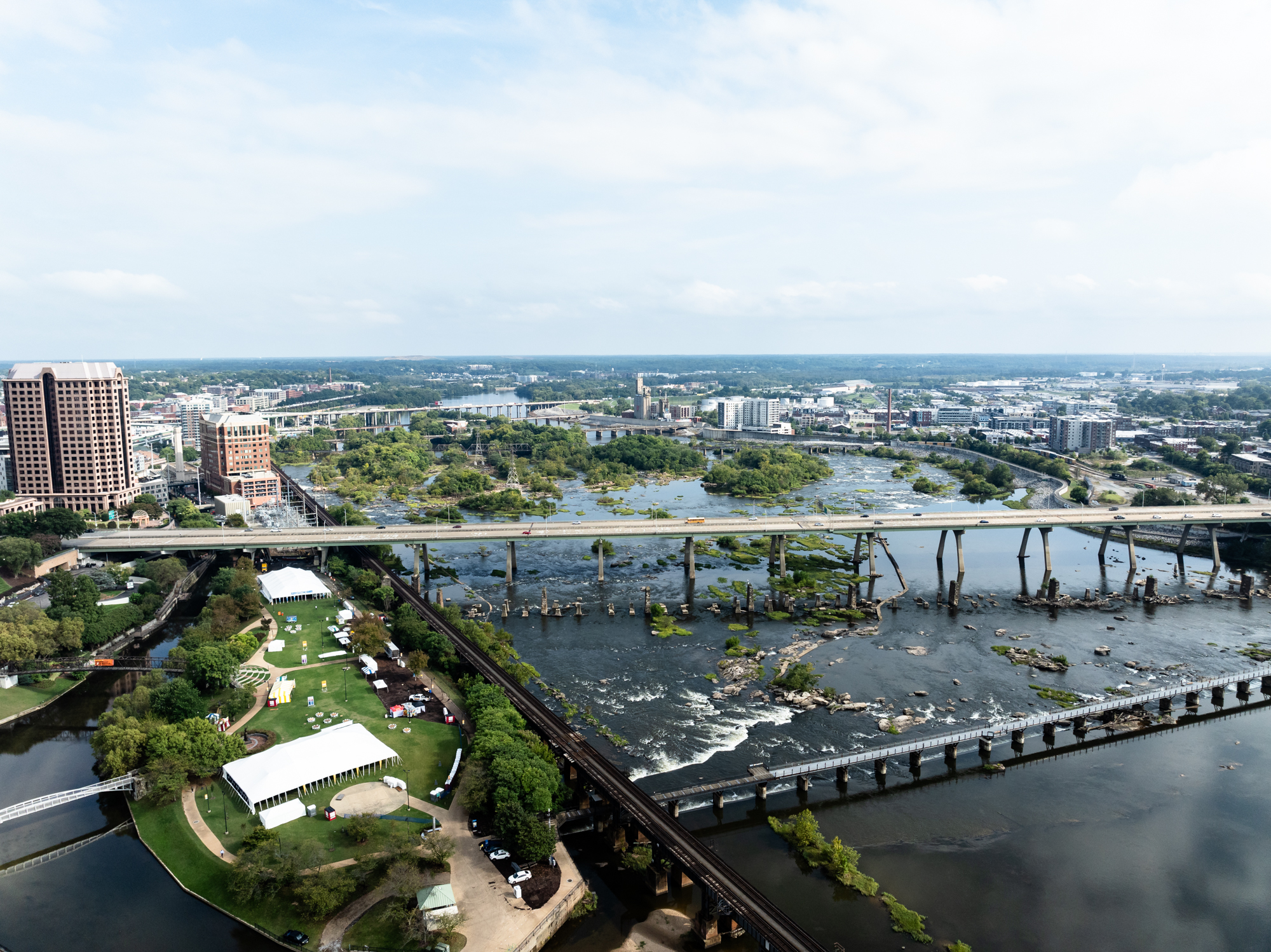 Aerial view of city, bridges, river, tents, and green spaces.