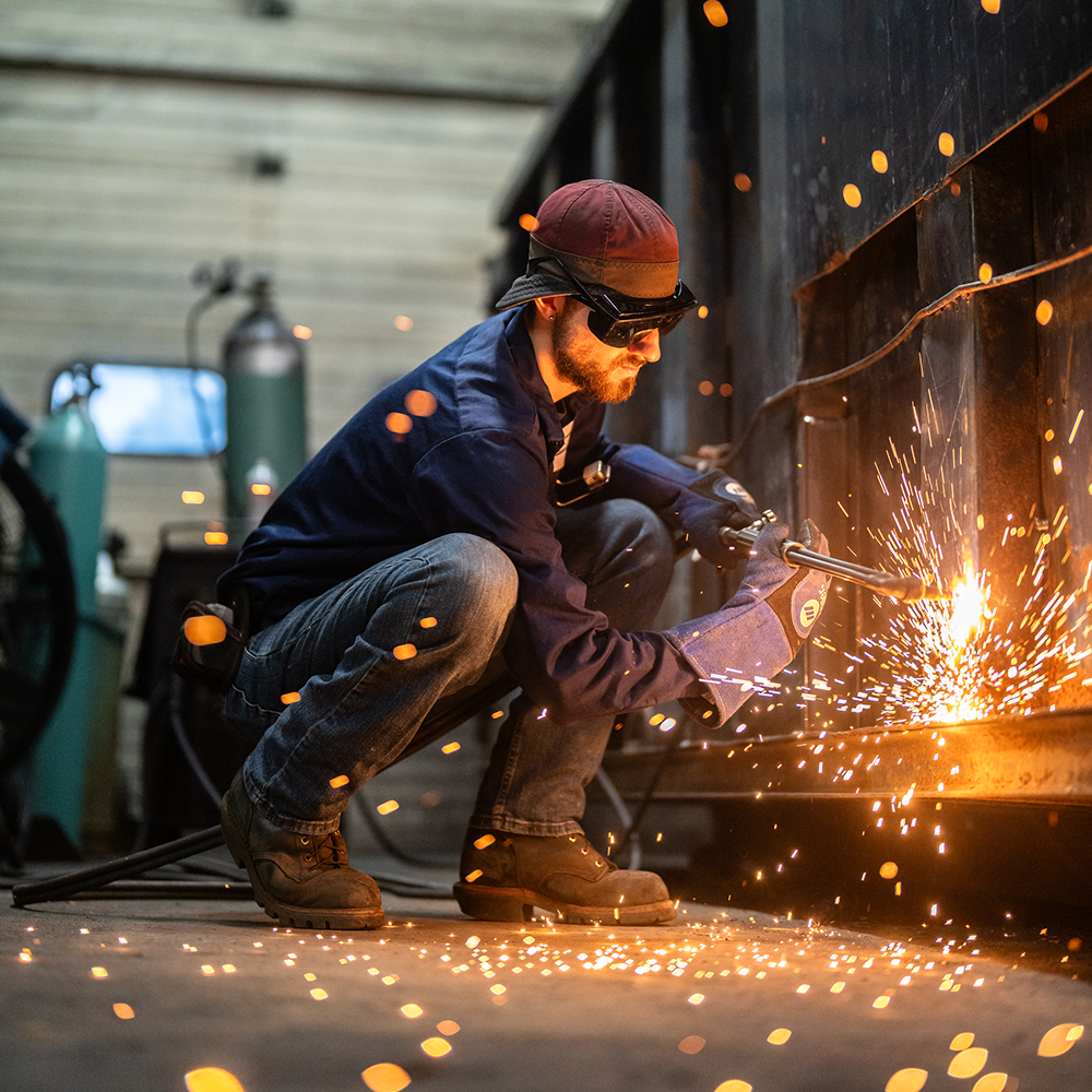 Worker in safety gear welding with sparks.