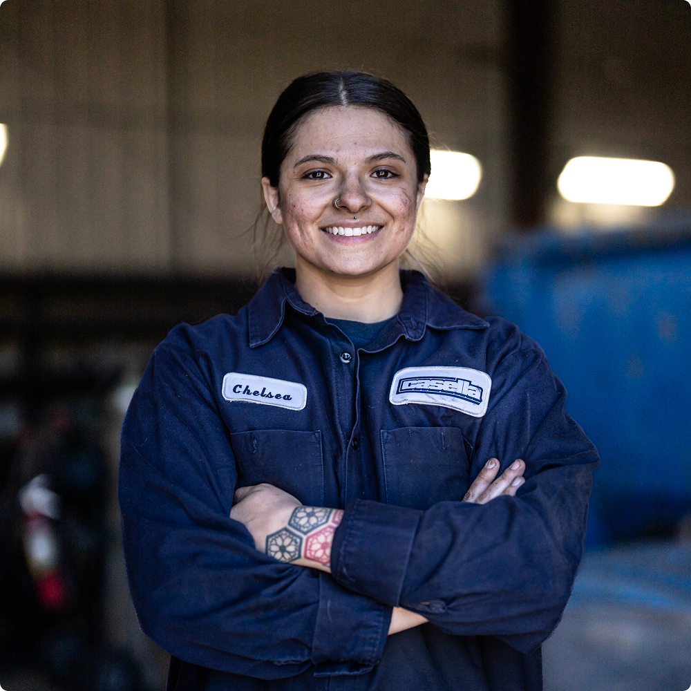 Smiling worker named Chelsea, dirty face and hands, arms crossed.