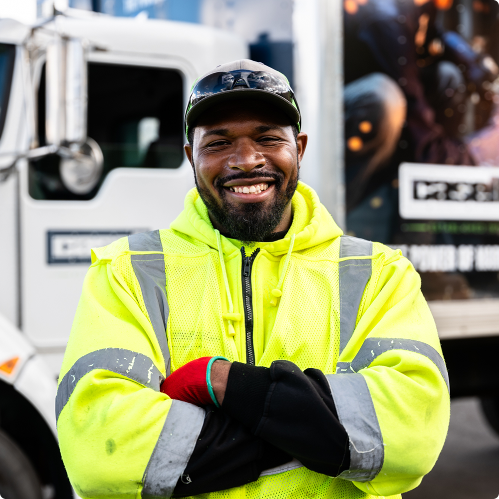 Man in neon yellow jacket and gloves smiles by white truck.