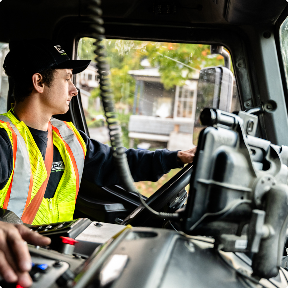 Man in safety vest drives truck, looking out window.