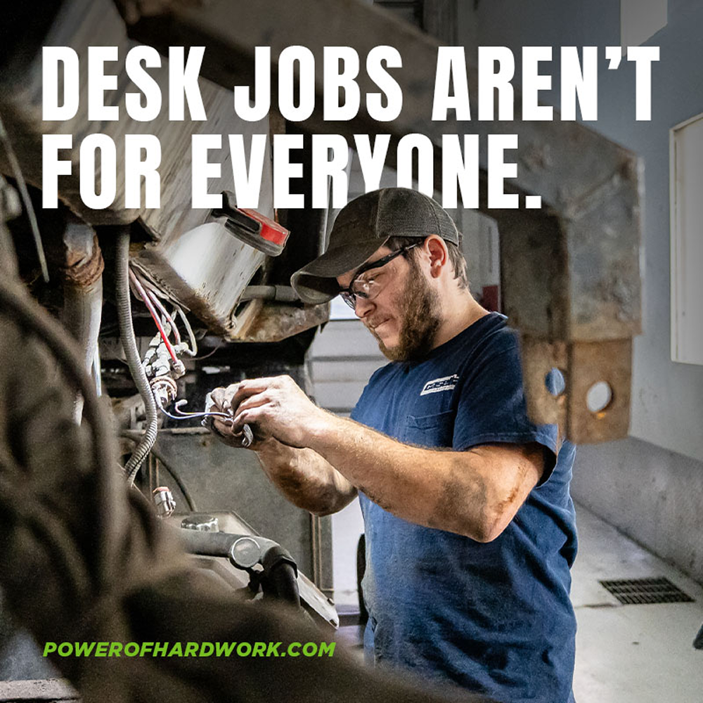 Man in work clothes repairs machine; text: “Desk jobs aren’t for everyone. powerofhardwork.com.”