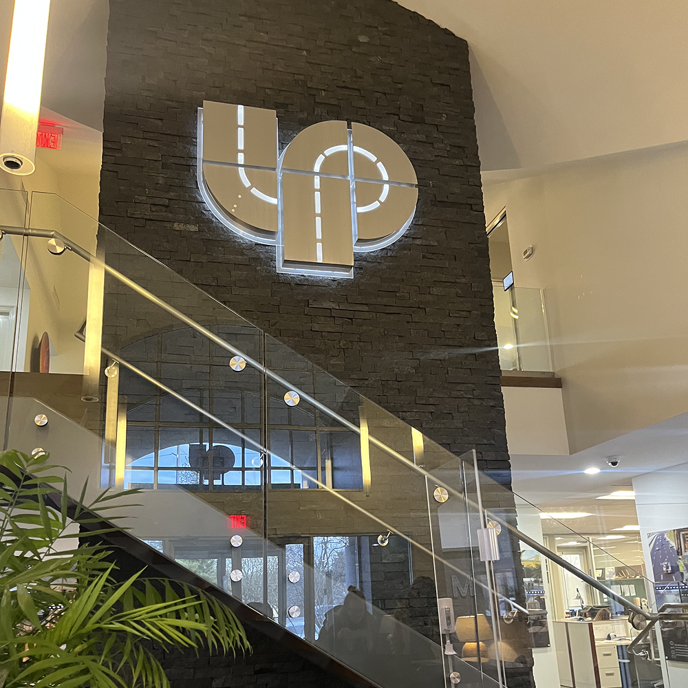 Glass staircase by stone wall with glowing logo.