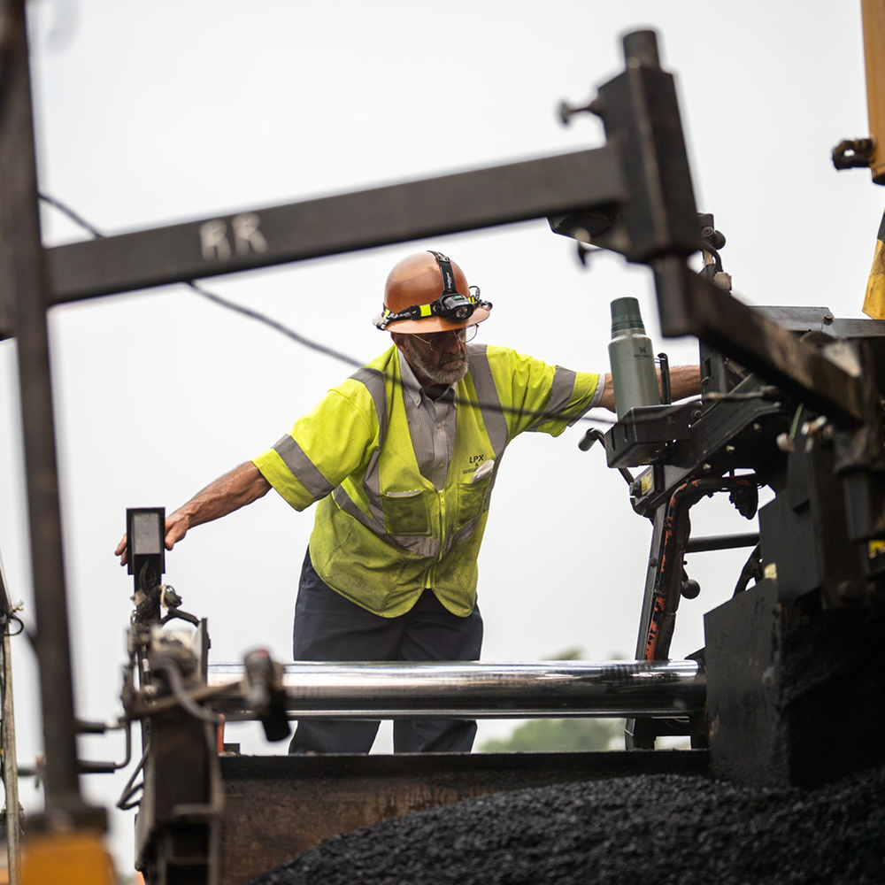 Worker in high-visibility gear operates machinery on roadwork site.