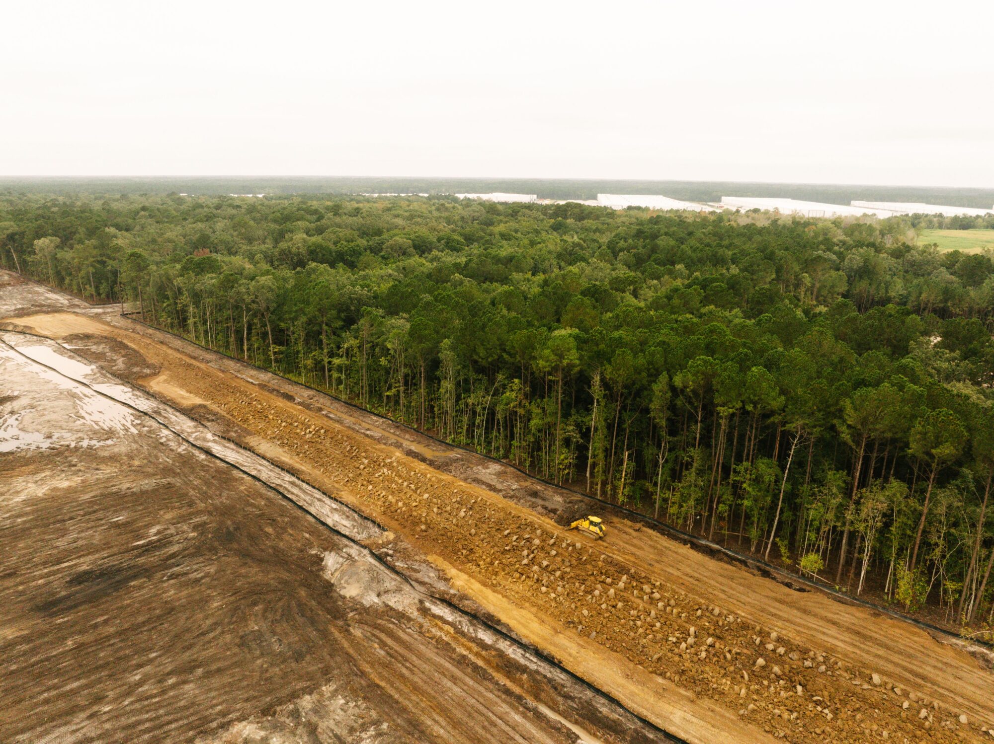 Aerial view: cleared land, dense forest, construction vehicles on dirt path.