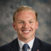 Blonde man smiling in a suite and blue tie.