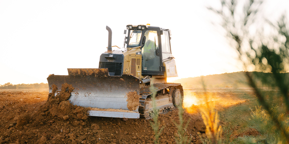 Bulldozer moves dirt at sunset amid dust and sunlight.