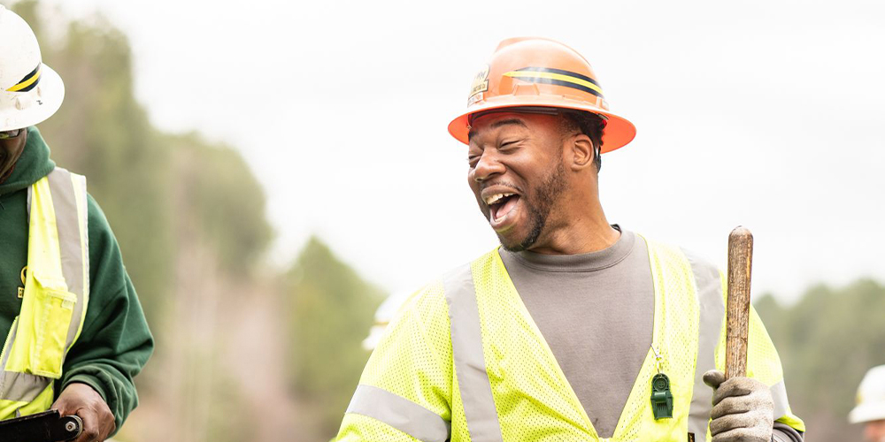 Smiling construction worker in safety vest and hard hat with shovel.